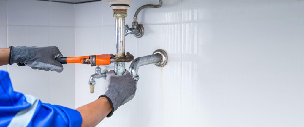 Technician plumber using a wrench to repair a water pipe under the sink.